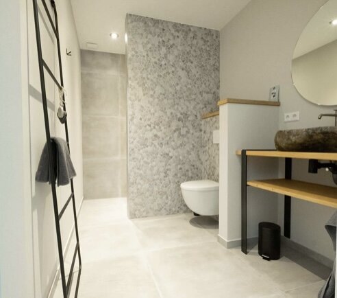 Badkamer met minerale wandafwerking, zwevend toilet en houten wastafelblad